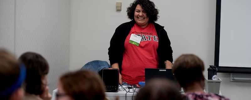 Female speaking in front of a classroom of people.